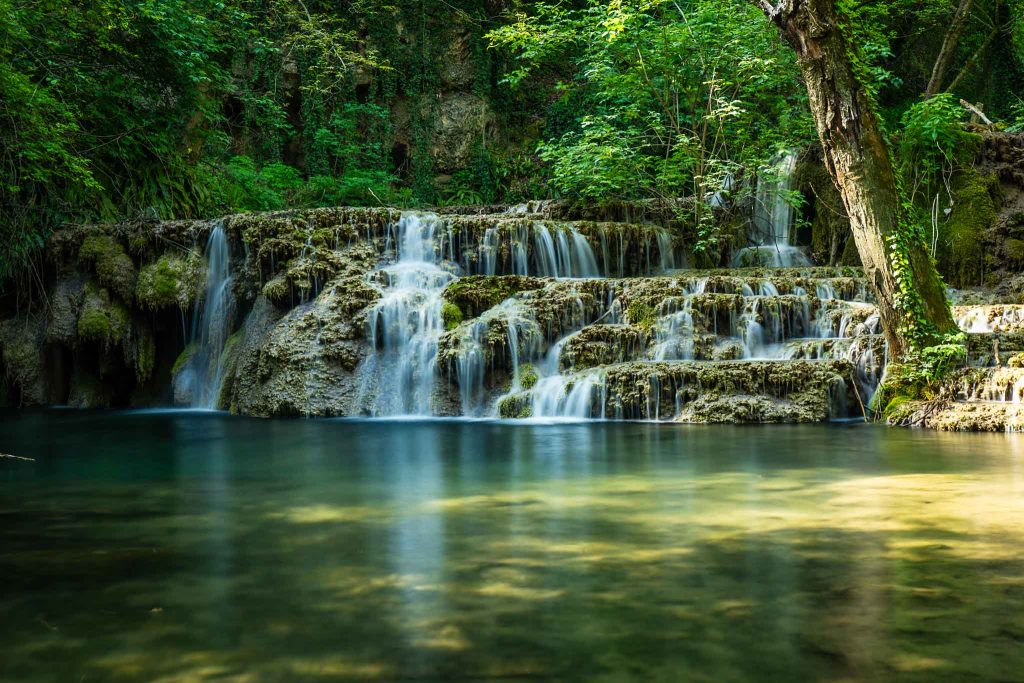 Turquoise cascades of Krushuna Falls in northern Bulgaria, surrounded by lush greenery.