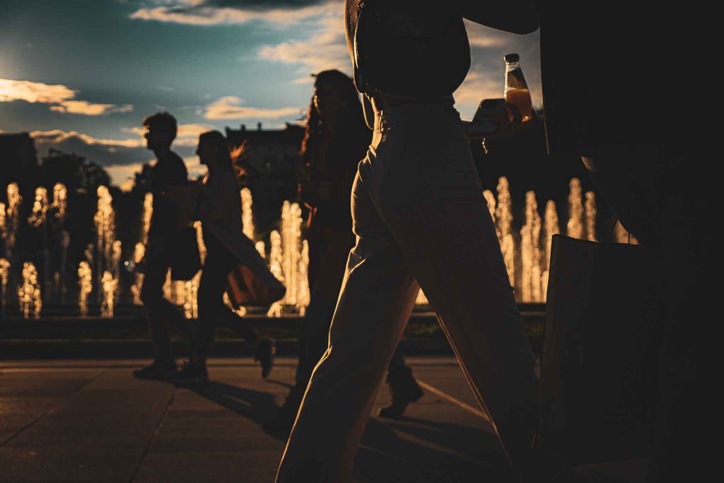 Backlit silhouettes of people walking through NDK square in Sofia, Bulgaria, during golden hour.