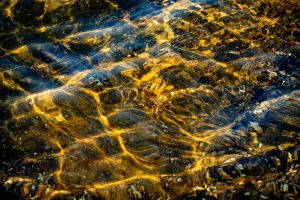 Warm golden sunlight flooding through shallow water over rounded pebbles, spreading across the entire surface.